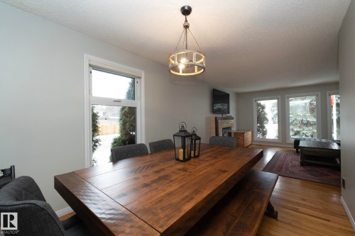 This inviting dining area features a large wooden table, a stylish overhead light fixture, and windows providing outdoor views - 54 Beaverbrook Crescent, St. Albert, AB - Indoor Photo Showing Dining Room