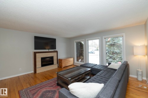 Living area featuring hardwood floors, a modern fireplace with a light-toned surround, and large windows that provide natural light - 54 Beaverbrook Crescent, St. Albert, AB - Indoor Photo Showing Living Room With Fireplace