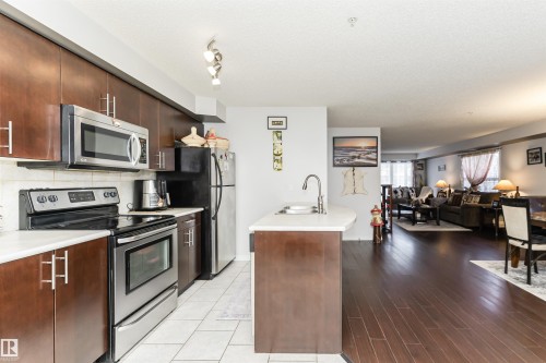Kitchen featuring stainless steel appliances, dark wood cabinetry, white countertops, and an island with a sink - 107 10118 106 Avenue, Edmonton, AB - Indoor Photo Showing Kitchen