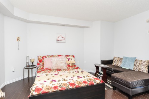 This versatile room features dark wood flooring and a neutral color palette, offering a bright and adaptable living space - 107 10118 106 Avenue, Edmonton, AB - Indoor Photo Showing Bedroom