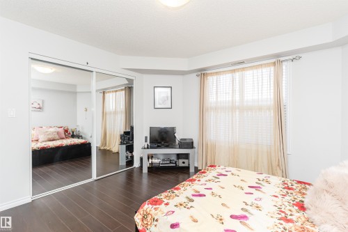 This room features dark wood flooring, a window with blinds and curtains, and a large closet with mirrored sliding doors - 107 10118 106 Avenue, Edmonton, AB - Indoor Photo Showing Bedroom