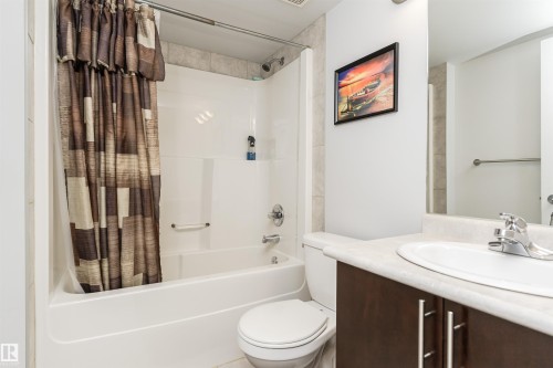 The bathroom features a bathtub with a shower, a toilet, and a vanity with a sink and storage below - 107 10118 106 Avenue, Edmonton, AB - Indoor Photo Showing Bathroom