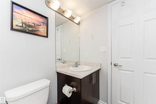 A well-appointed bathroom featuring a white toilet, a vanity with an integrated sink, and a mirror with overhead lighting - 107 10118 106 Avenue, Edmonton, AB - Indoor Photo Showing Bathroom