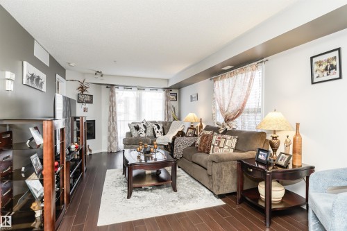 The spacious living area features rich hardwood flooring, a decorative fireplace, and large windows with sheer curtains - 107 10118 106 Avenue, Edmonton, AB - Indoor Photo Showing Living Room