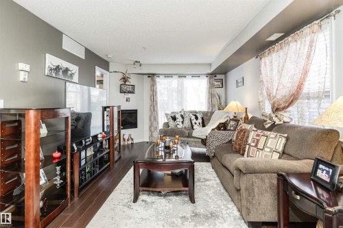 Living room featuring hardwood flooring, a fireplace, and large windows providing natural light - 107 10118 106 Avenue, Edmonton, AB - Indoor Photo Showing Living Room With Fireplace