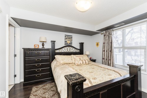 This bedroom features dark hardwood floors and a large window with blinds, providing natural light - 107 10118 106 Avenue, Edmonton, AB - Indoor Photo Showing Bedroom