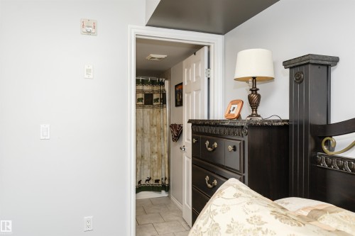 The bedroom features a dark wood dresser with ornate details and a matching headboard - 107 10118 106 Avenue, Edmonton, AB - Indoor
