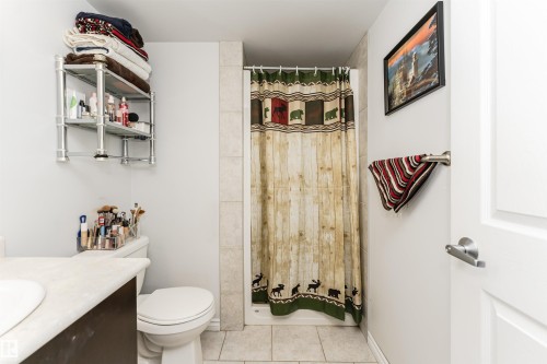 Bathroom featuring a shower with tiled walls, a toilet, and a vanity with a light-colored countertop and an integrated sink - 107 10118 106 Avenue, Edmonton, AB - Indoor Photo Showing Bathroom