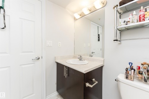 Bathroom featuring a vanity with a dark wood-look cabinet, a light-colored countertop, and a built-in sink - 107 10118 106 Avenue, Edmonton, AB - Indoor Photo Showing Bathroom