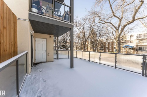 Spacious outdoor patio area featuring a white door entrance, glass panel railing, and a privacy wall - 107 10118 106 Avenue, Edmonton, AB - Outdoor With Exterior
