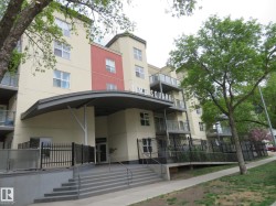 Modern multi-story building featuring a prominent covered entrance and a mix of light-colored and red exterior finishes - 