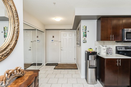 The property features a kitchen with dark wood cabinetry, a tiled backsplash, and stainless steel appliances - 107 10118 106 Avenue, Edmonton, AB - Indoor Photo Showing Kitchen