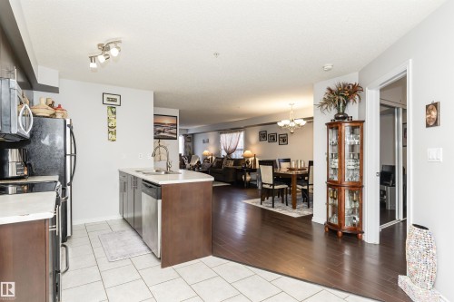 The property features a kitchen with light-colored tile flooring and dark wood cabinetry - 107 10118 106 Avenue, Edmonton, AB - Indoor Photo Showing Kitchen With Double Sink