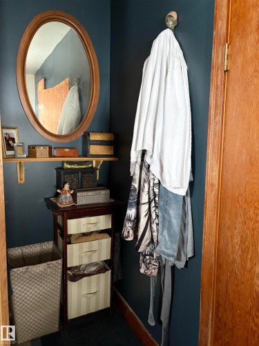 This compact area features a round wooden-framed mirror, a small wooden shelf, and a dark wooden cabinet with three striped storage drawers - 5117 52 Avenue, Elk Point, AB - Indoor Photo Showing Other Room