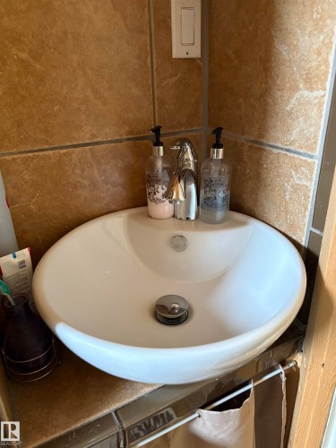 Bathroom vanity featuring a white oval vessel sink with a chrome faucet, set against a backdrop of brown tiled walls - 5117 52 Avenue, Elk Point, AB - Indoor Photo Showing Bathroom