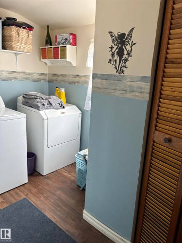 This utility area features durable wood-look flooring and a functional wall shelf for storage - 5117 52 Avenue, Elk Point, AB - Indoor Photo Showing Laundry Room