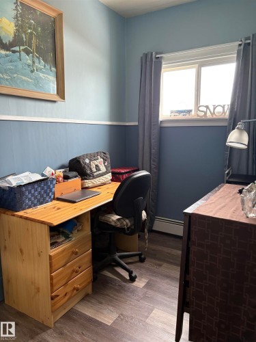 This room features light blue walls with a darker blue wainscoting, grey window treatments, and durable-looking flooring. It can be used for an office, bedroom, or craft room. - 5117 52 Avenue, Elk Point, AB - Indoor Photo Showing Office