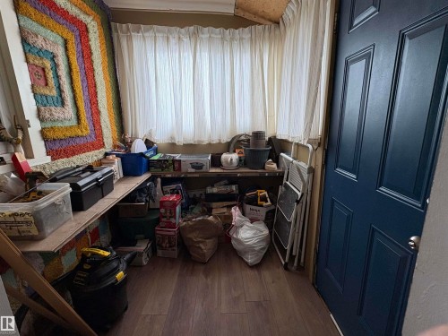 This versatile space features a window with white curtains, wood-look flooring, and a dark blue paneled door. - 5117 52 Avenue, Elk Point, AB - Indoor