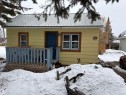 The property features yellow siding, a metal roof, and a front porch with a blue railing. Fenced back yard with parking spaces behind. - 5117 52 Avenue, Elk Point, AB  - Outdoor With Exterior 
