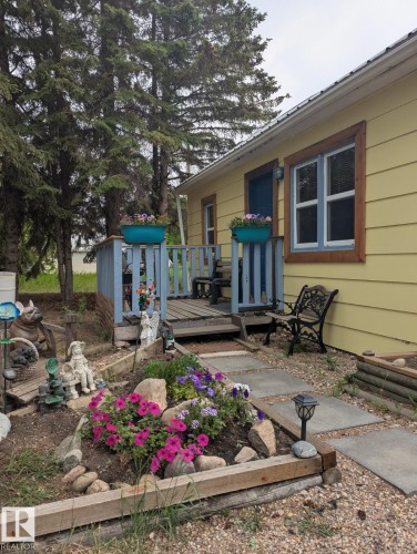The property features a charming front exterior with yellow siding and a welcoming porch. Beautiful flower garden. - 5117 52 Avenue, Elk Point, AB - Outdoor