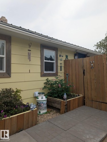 The exterior features yellow siding, white-framed windows with rustic wooden trim, and a private wooden fence. - 5117 52 Avenue, Elk Point, AB - Outdoor With Exterior