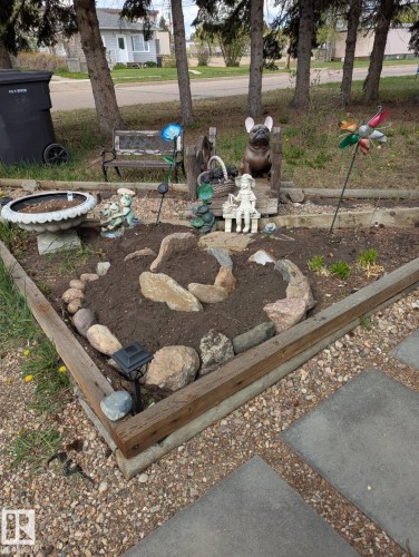 The property features an established garden bed with a wooden border, natural rock accents, and a variety of garden ornaments - 5117 52 Avenue, Elk Point, AB - Outdoor