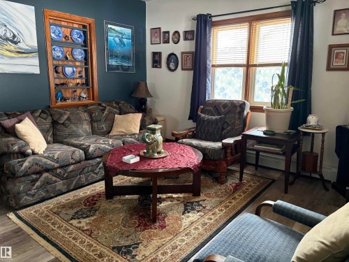 Living area featuring a patterned area rug, a window with blinds and curtains, and wood-toned flooring. - 5117 52 Avenue, Elk Point, AB - Indoor Photo Showing Living Room