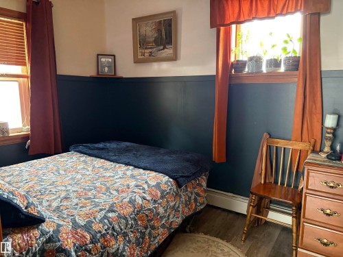 This room features dark-toned wainscoting and light-toned walls, complemented by two windows with valances and full-length curtains. - 5117 52 Avenue, Elk Point, AB - Indoor Photo Showing Bedroom