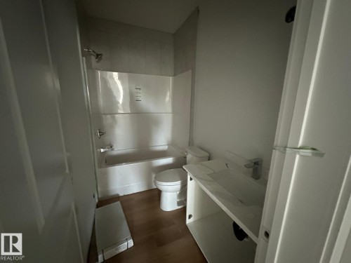 Bathroom featuring a white bathtub, shower with a chrome shower head, a white toilet, and a vanity with a white sink and chrome faucet, all complemented by wood-look flooring - 9214 152 Street, Edmonton, AB - Indoor Photo Showing Bathroom