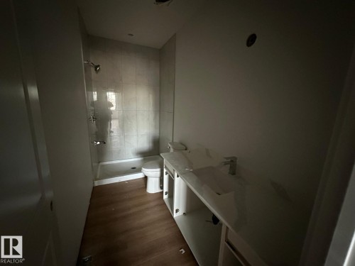 Bathroom featuring a tiled shower with a glass panel, a toilet, a vanity with a countertop and integrated sink, and wood-look flooring - 9214 152 Street, Edmonton, AB - Indoor Photo Showing Other Room
