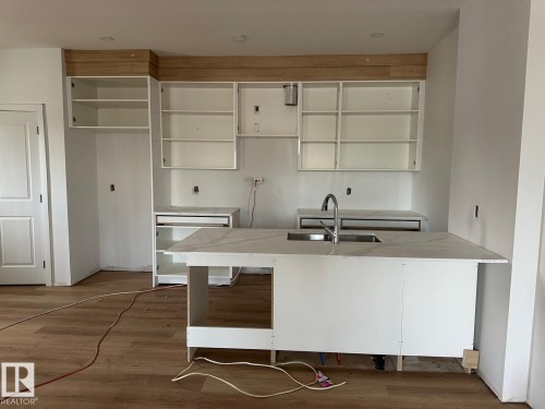 The kitchen area features light-colored flooring, white cabinetry, and a central island with a sink and a light-colored countertop - 9214 152 Street, Edmonton, AB - Indoor Photo Showing Kitchen With Double Sink