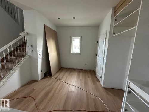 This interior space features light-colored flooring, a window, and a staircase with white railings - 9214 152 Street, Edmonton, AB - Indoor Photo Showing Other Room