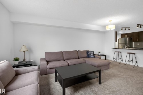 Open concept living area featuring light-colored carpeting, a kitchen bar with dark countertops, and dark kitchen cabinetry - 311 12035 22 Avenue, Edmonton, AB - Indoor Photo Showing Living Room