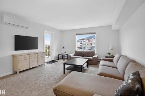 Living area featuring a large window with views of surrounding buildings, and a door leading to an outdoor balcony - 311 12035 22 Avenue, Edmonton, AB - Indoor Photo Showing Living Room
