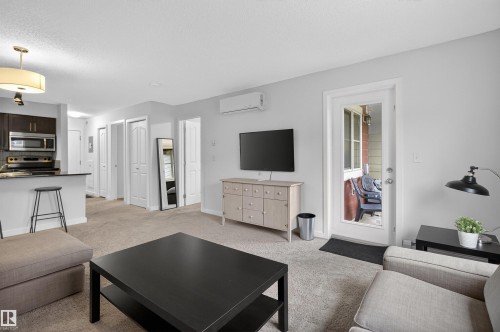 Open concept living area featuring light gray walls, carpet flooring, and a glass-paneled door leading to an outdoor space - 311 12035 22 Avenue, Edmonton, AB - Indoor Photo Showing Living Room