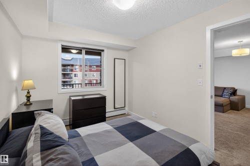 This bright room features a window with a view of other residential buildings, providing natural light, and textured ceilings - 311 12035 22 Avenue, Edmonton, AB - Indoor