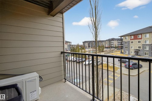 The property features a balcony with a black metal railing and a concrete floor, offering views of the surrounding residential buildings and a parking area - 311 12035 22 Avenue, Edmonton, AB - Outdoor With Balcony With Exterior