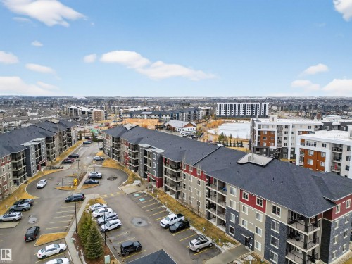 This property offers a modern exterior design with a dark shingle roof, complemented by red, grey, and stone-accented facades - 311 12035 22 Avenue, Edmonton, AB - Outdoor With View