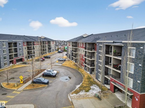 The property features multi-story buildings with balconies, a paved parking area, and an exterior of stone and siding - 311 12035 22 Avenue, Edmonton, AB - Outdoor With Balcony