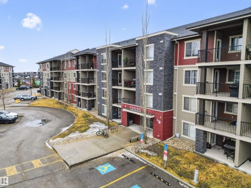 This multi-story residential building features a contemporary design with balconies, a prominent main entrance, and a parking area - 311 12035 22 Avenue, Edmonton, AB - Outdoor With Balcony