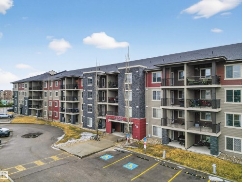 The property features a multi-story building with balconies, a dark-toned roof, and a paved parking area - 311 12035 22 Avenue, Edmonton, AB - Outdoor With Balcony With Facade