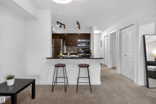 Contemporary open-concept living space featuring a kitchen with stainless steel appliances, dark cabinetry, and a breakfast bar - 311 12035 22 Avenue, Edmonton, AB - Indoor Photo Showing Kitchen