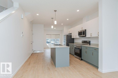 The open concept kitchen features a central island with a sink, stainless steel appliances, and two-tone cabinetry - 9652 Colak Link Link, Edmonton, AB - Indoor Photo Showing Kitchen