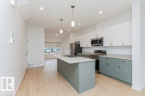 Kitchen featuring an island with a sink, stainless steel appliances, and two-tone cabinetry with white upper cabinets and grey lower cabinets - 9652 Colak Link Link, Edmonton, AB - Indoor Photo Showing Kitchen