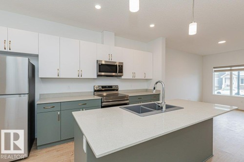 The kitchen features white upper cabinetry paired with contrasting lower cabinetry, stainless steel appliances, and a central island with a double sink and an extendable countertop - 9652 Colak Link Link, Edmonton, AB - Indoor Photo Showing Kitchen With Double Sink With Upgraded Kitchen