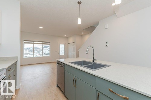 Modern kitchen featuring a double basin sink with a chrome faucet, light-colored countertops, and teal-colored cabinetry - 9652 Colak Link Link, Edmonton, AB - Indoor Photo Showing Kitchen With Double Sink