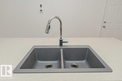 Kitchen sink featuring a dual basin, a chrome faucet with a pull-down sprayer, and a light-colored countertop - 9652 Colak Link Link, Edmonton, AB - Indoor Photo Showing Kitchen With Double Sink