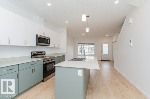 The property features an open concept kitchen with white upper cabinetry, light blue lower cabinetry, stainless steel appliances, and a central island with a sink and pendant lighting - 9652 Colak Link Link, Edmonton, AB - Indoor Photo Showing Kitchen With Double Sink