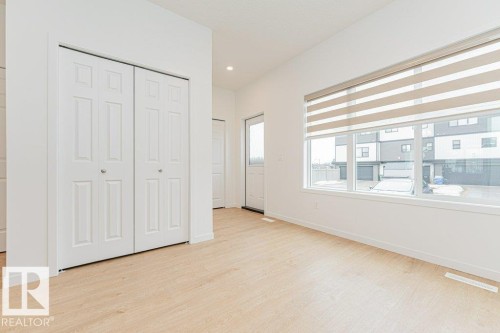 This room features light-colored flooring, white walls, and a large window with blinds - 9652 Colak Link Link, Edmonton, AB - Indoor Photo Showing Other Room