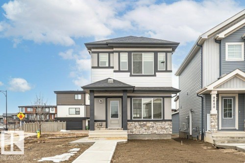 This property features a contemporary exterior with white siding, dark trim, and a stone accent facade - 9652 Colak Link Link, Edmonton, AB - Outdoor With Facade